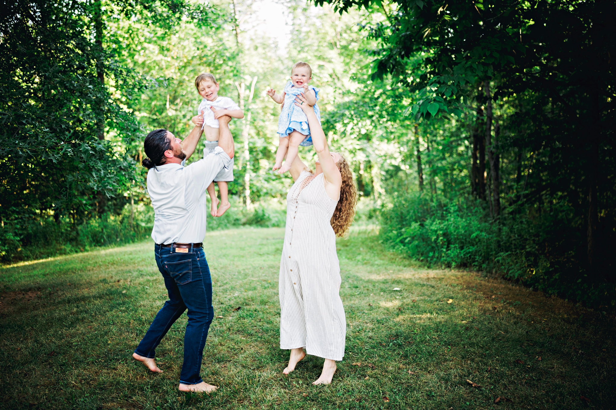Mom and Dad gently tossing their young children into the air for maximum smiles in an open field.